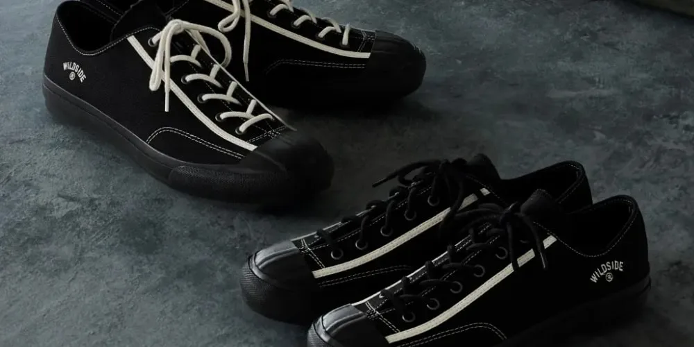 Deux paires de baskets noires sur le sol sombre.