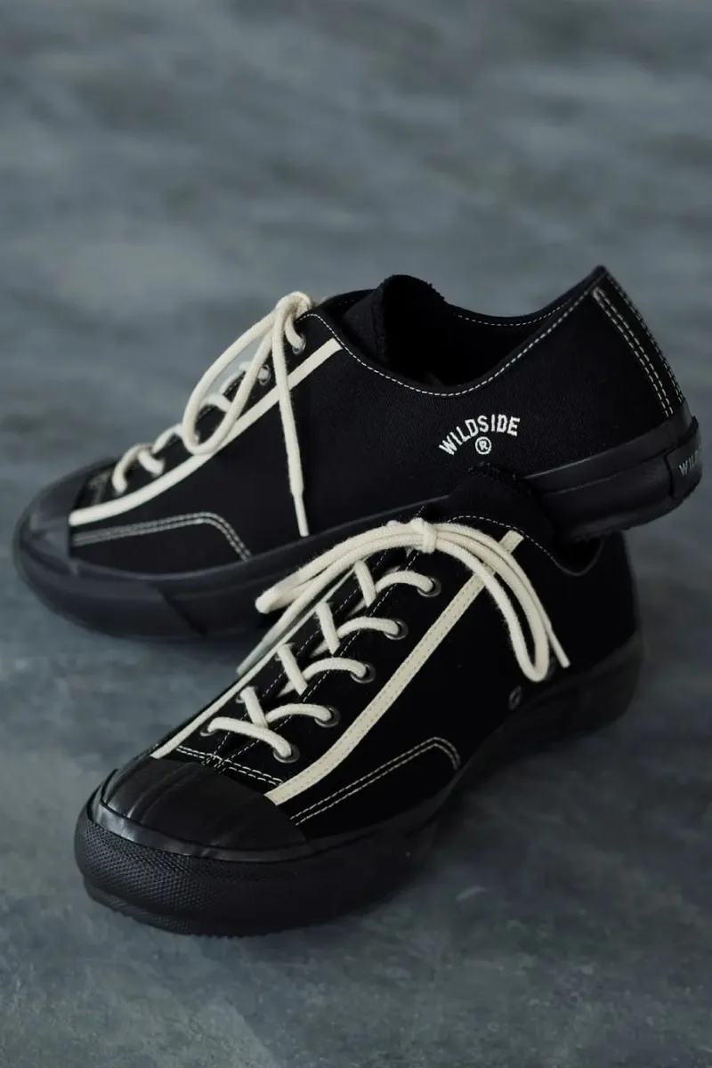 Chaussures noires avec semelles en caoutchouc et lacets blancs sur fond gris.