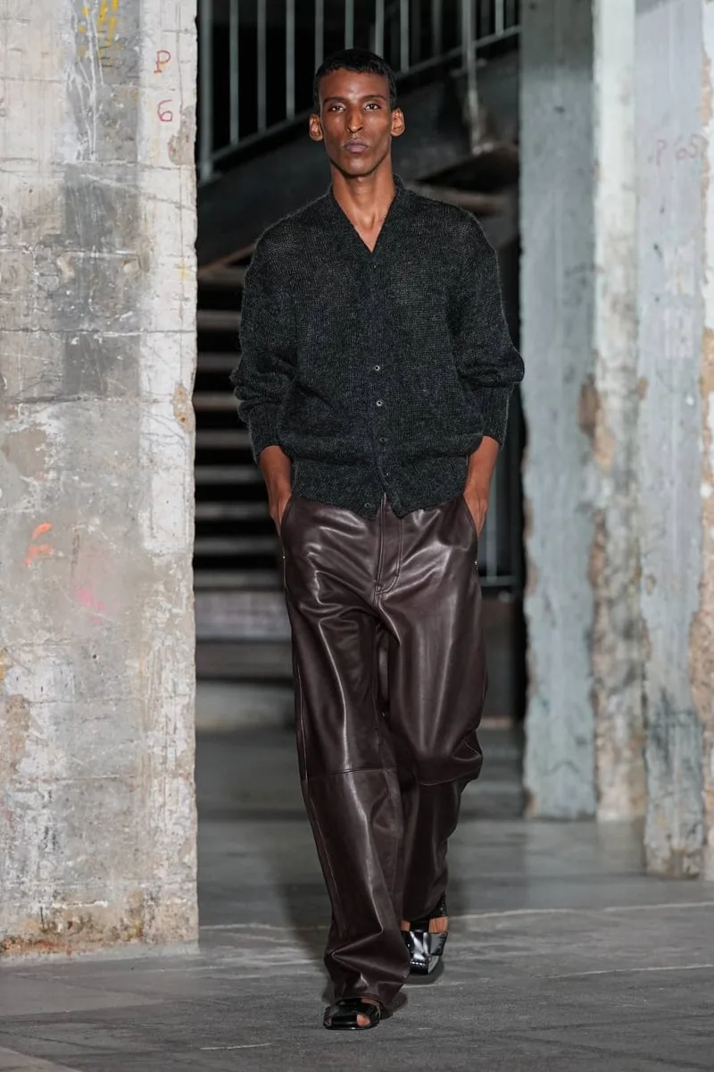 Homme portant un cardigan et pantalon en cuir marron, intérieur urbain.