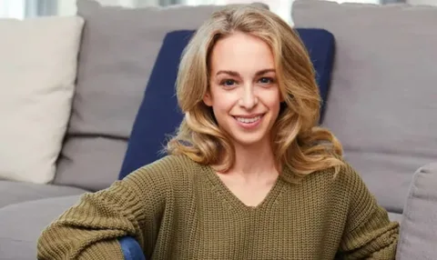 Femme souriante assise sur un canapé avec un pull vert.