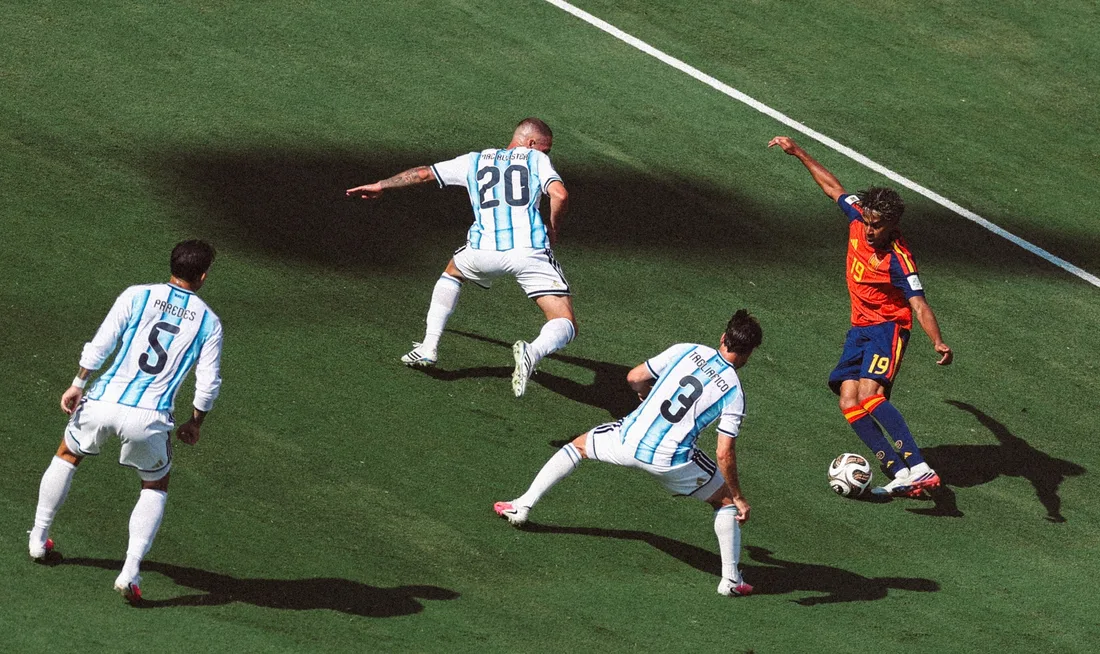 Quatre joueurs de football sur le terrain, trois en blanc et un en rouge et bleu.