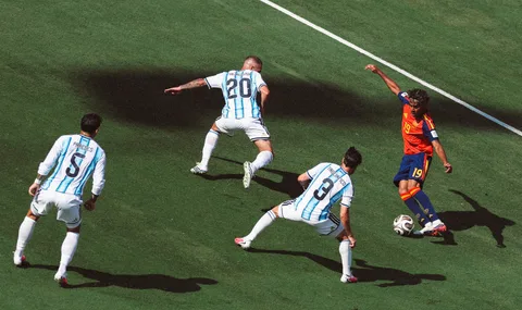 Quatre joueurs de football sur le terrain, trois en blanc et un en rouge et bleu.