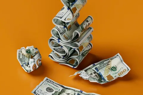 Des billets de cent dollars pliés et froissés sur un fond orange.