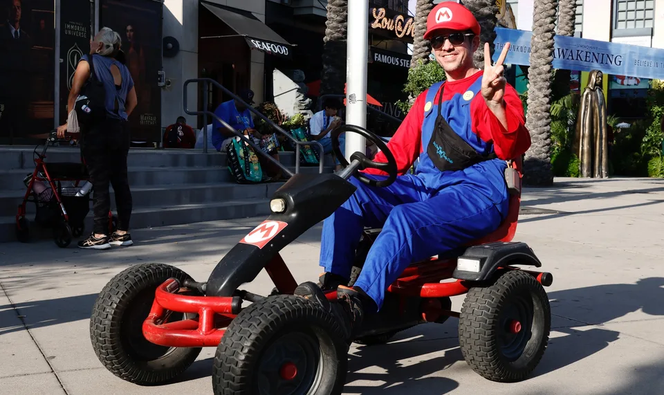 Homme en costume de Mario sur un kart, faisant le signe de la paix à l'extérieur.