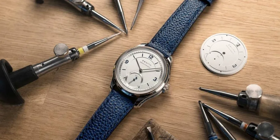 Montre avec bracelet bleu et outils d'horlogerie sur un plan de travail en bois.