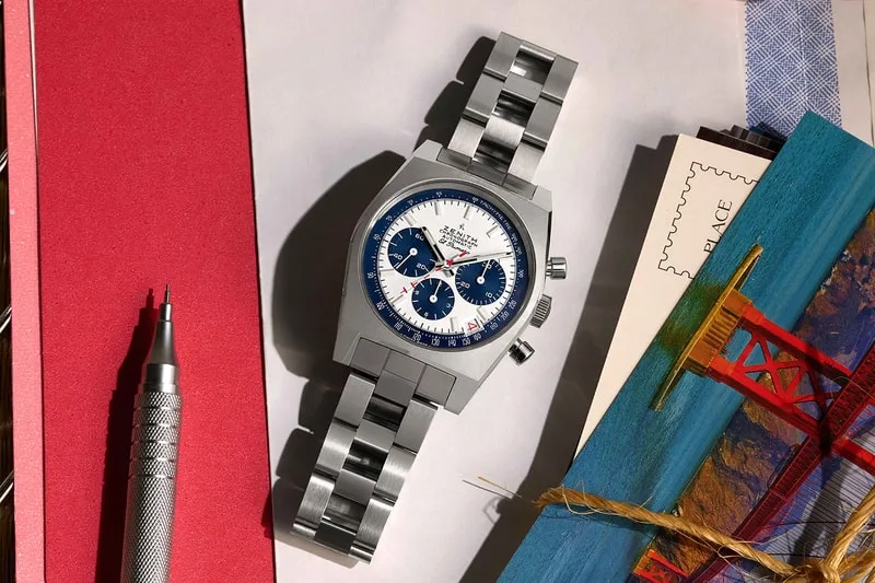 Montre argentée avec cadran bleu et blanc, posée sur des cartes postales.
