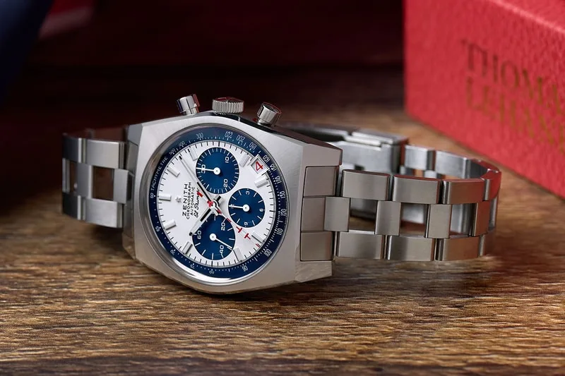 Montre en acier inoxydable avec cadran bleu et blanc sur une surface en bois.